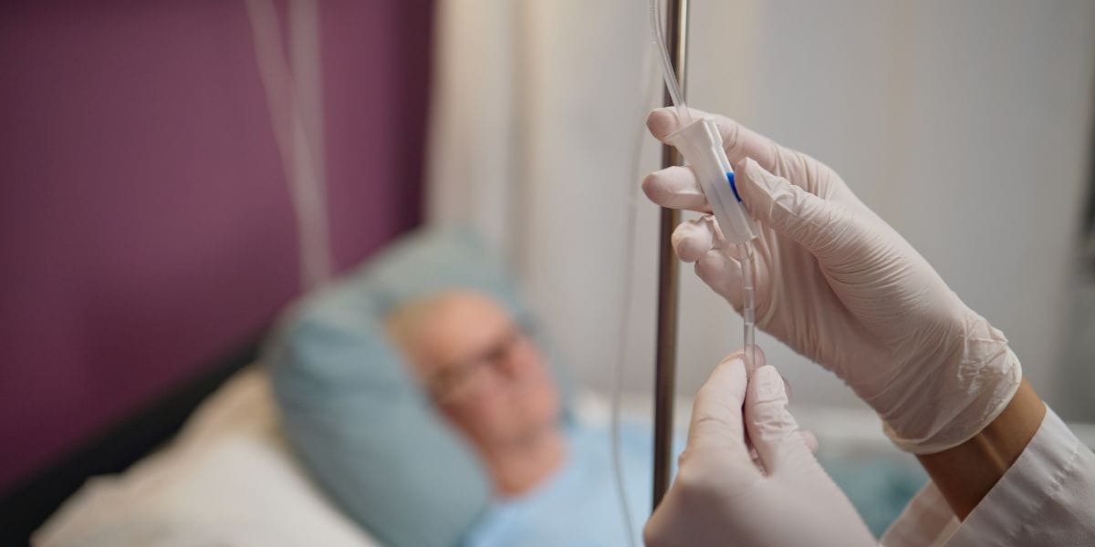 A patient in a hospital bed holds a medical tube, appearing calm and attentive to their surroundings.