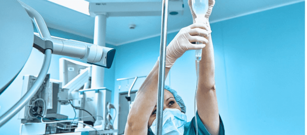 A woman in a hospital gown holds a surgical instrument, preparing for a medical procedure in a clinical setting.