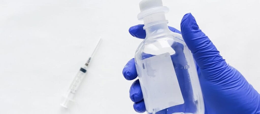 A person wearing blue gloves holds a syringe, preparing for a medical procedure or vaccination.