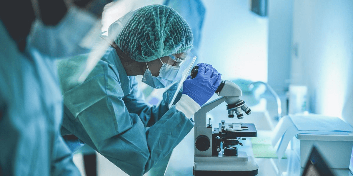 A laboratory professional in a white lab coat studies a microscope, conducting experiments and observations in a research lab.