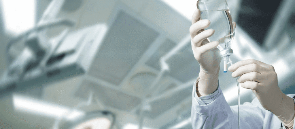 A doctor in a white coat holds a glass filled with a clear liquid, looking attentively at it.