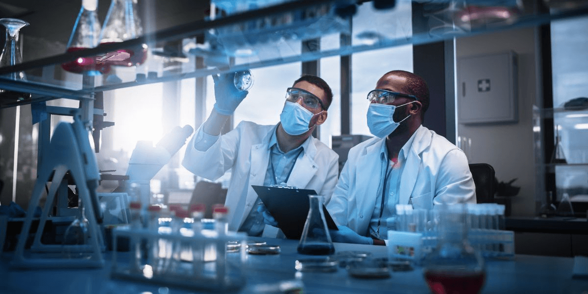 Two scientists in lab coats and masks collaborate on a research project in a laboratory setting.